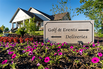 Flowers and sign with Golf & Events with arrow pointing right and Deliveries with arrow pointing left, with Event Center in background