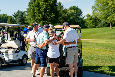 Group of friends on golf course embracing with man and golf carts in background